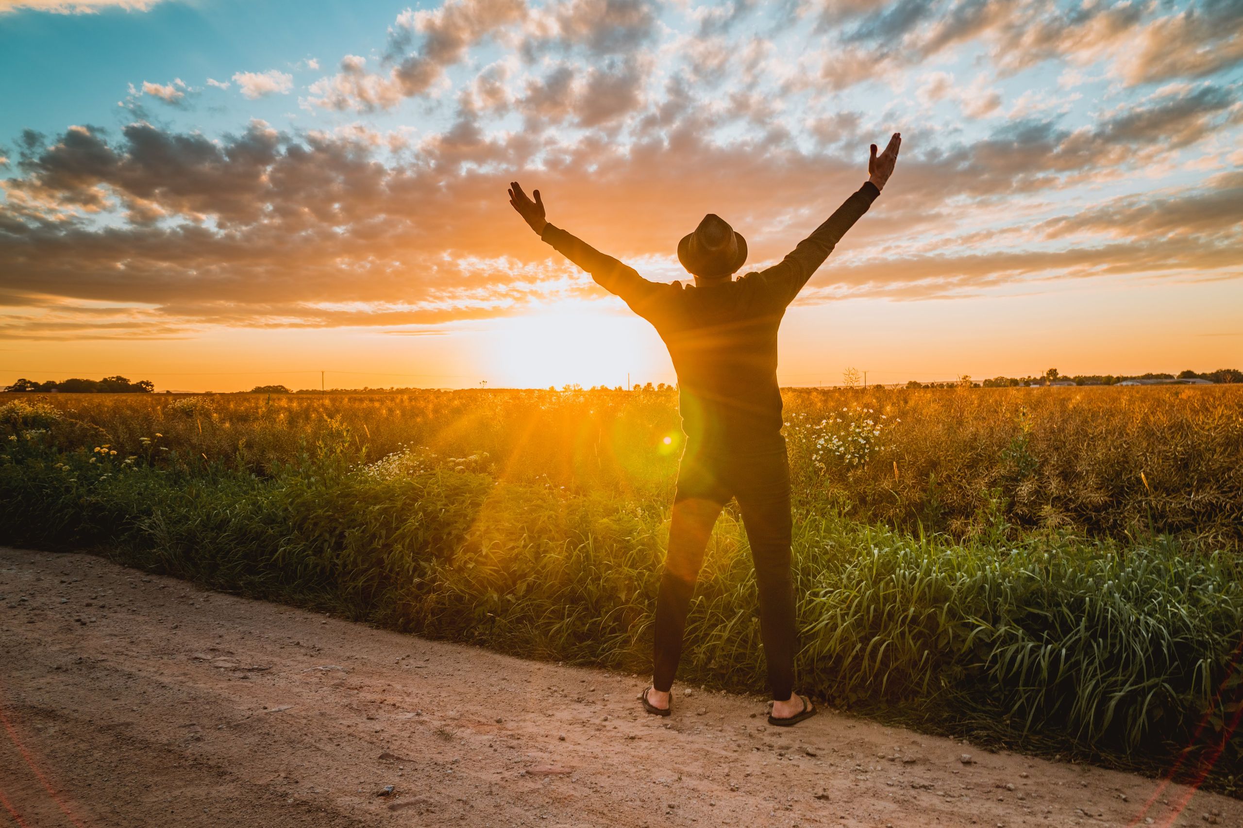 Photo by Peggy Anke - Racing Fans Dev A man raises arms in freedom at sunrise in a rural field, expressing joy and connection with nature.