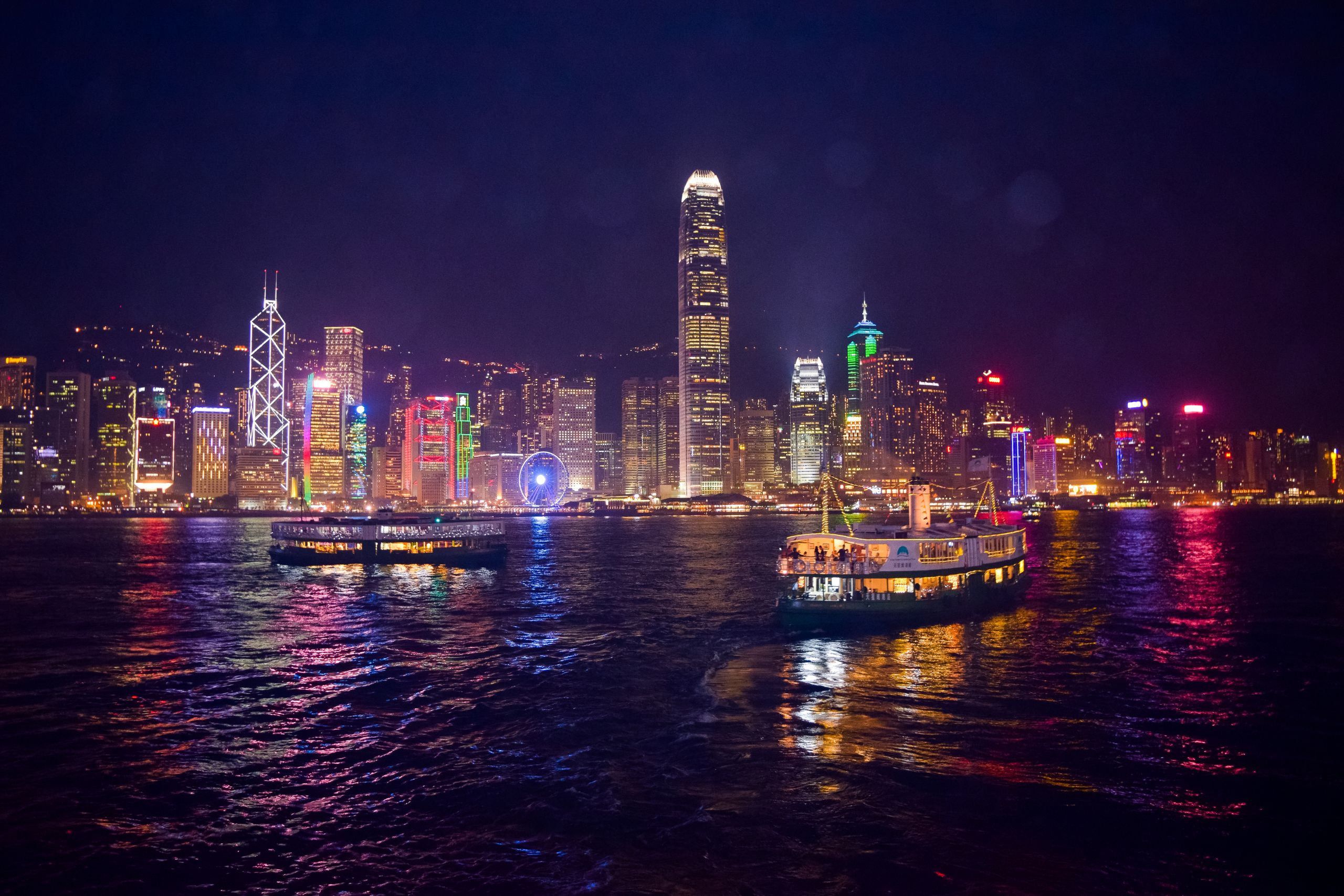 Photo by Julian Lobo - Racing Fans Dev Captivating night view of Hong Kong's illuminated skyline and ferries reflecting on the water.